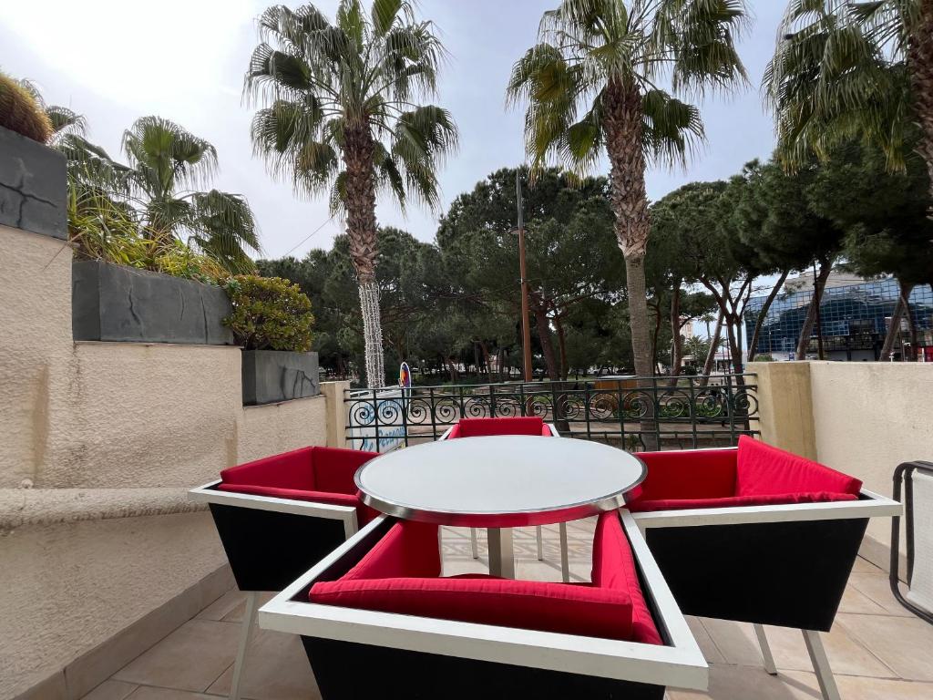 a table and red chairs on a balcony with palm trees at Appartement sur la Pinède à Juan les pins in Antibes