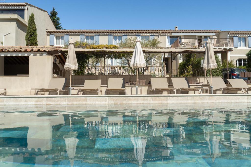 einen Pool in einem Hotel mit Stühlen und Sonnenschirmen in der Unterkunft Hôtel Le Pré Saint Michel in Manosque