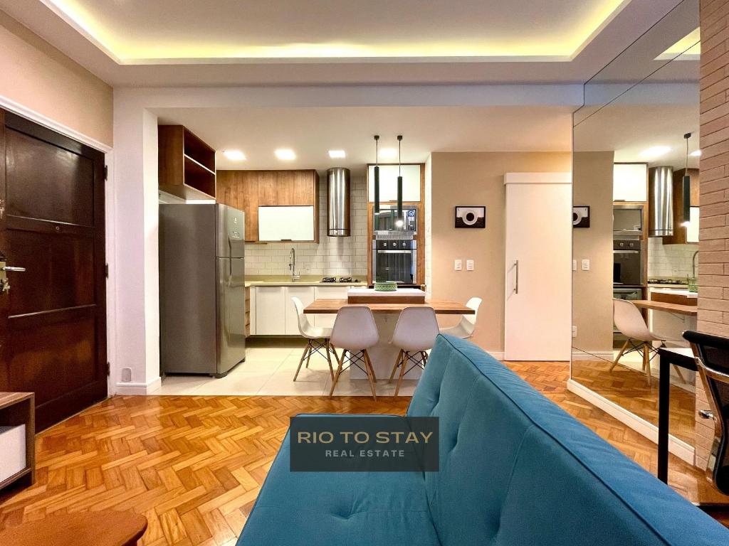 Hotel Reformado e charmoso próximo à praia do Leblon!, a living room with a blue couch and a kitchen at Renovated and charming close to Leblon beach! in Rio de Janeiro