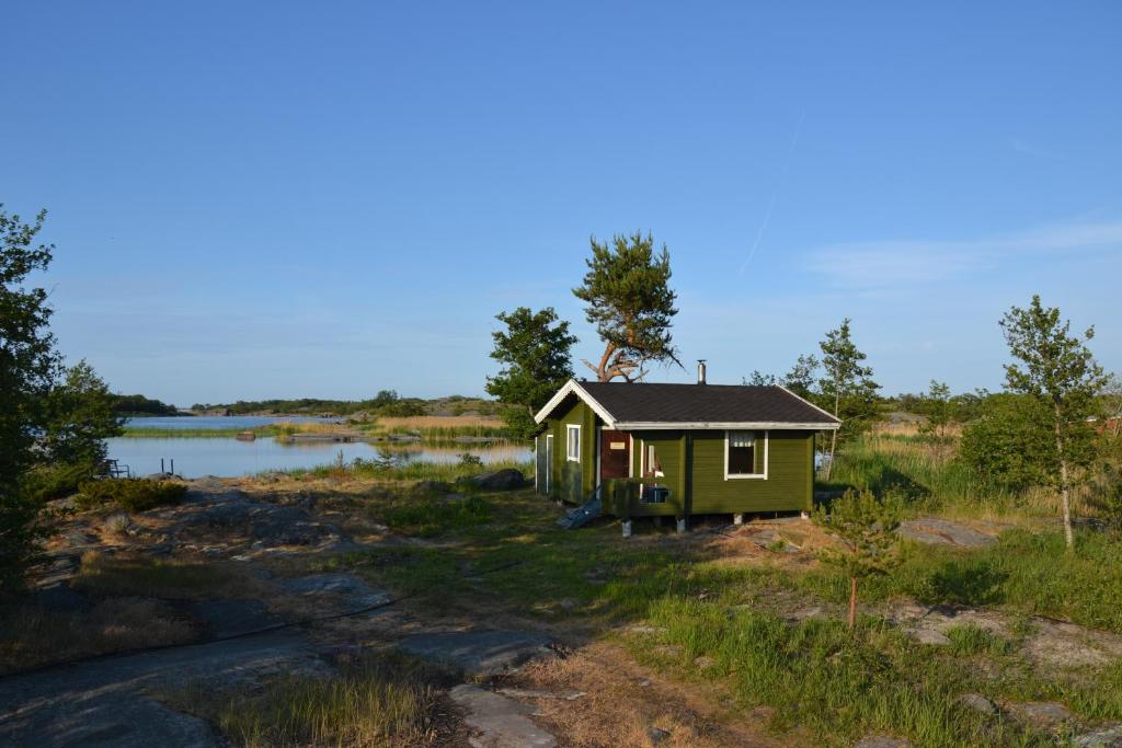 a small green cabin in a field next to a lake at Klobbars Gästhem o Stugor in Kökar