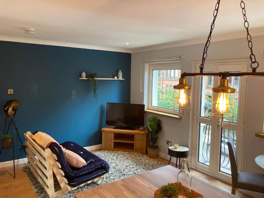 a living room with a blue wall and a tv at Rustic Top Floor West End Pad With Balcony, Parking next to Byers Road, Aston Lane, Glasgow Uni in Glasgow