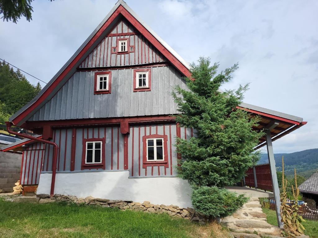 czerwona i szara stodoła z drzewem przed nią w obiekcie Roubenka Jizerka v horách Jizerských w mieście Tanvald