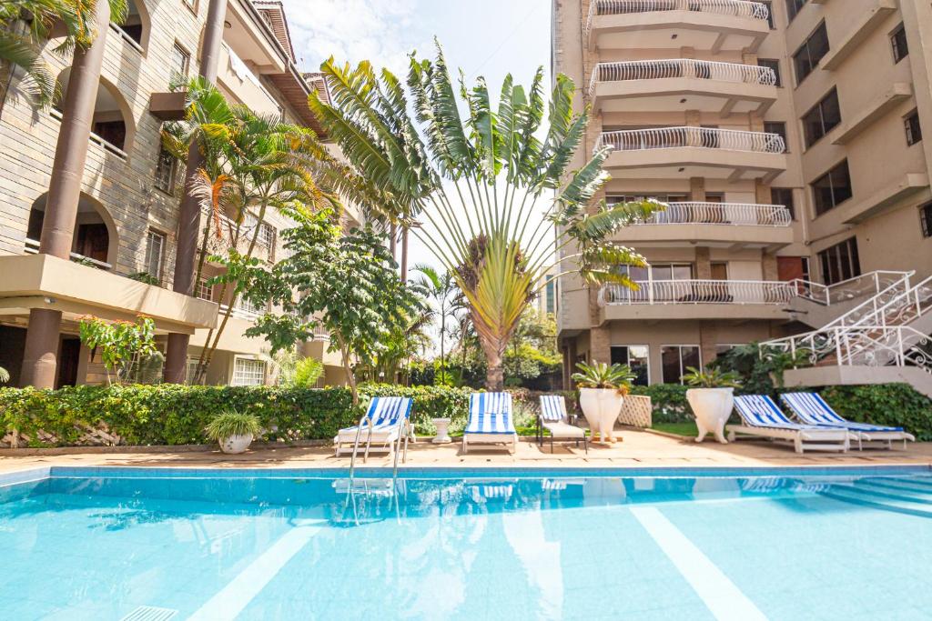 a swimming pool in front of a building with chairs and a palm tree at Eldon Suites & Apartments in Nairobi