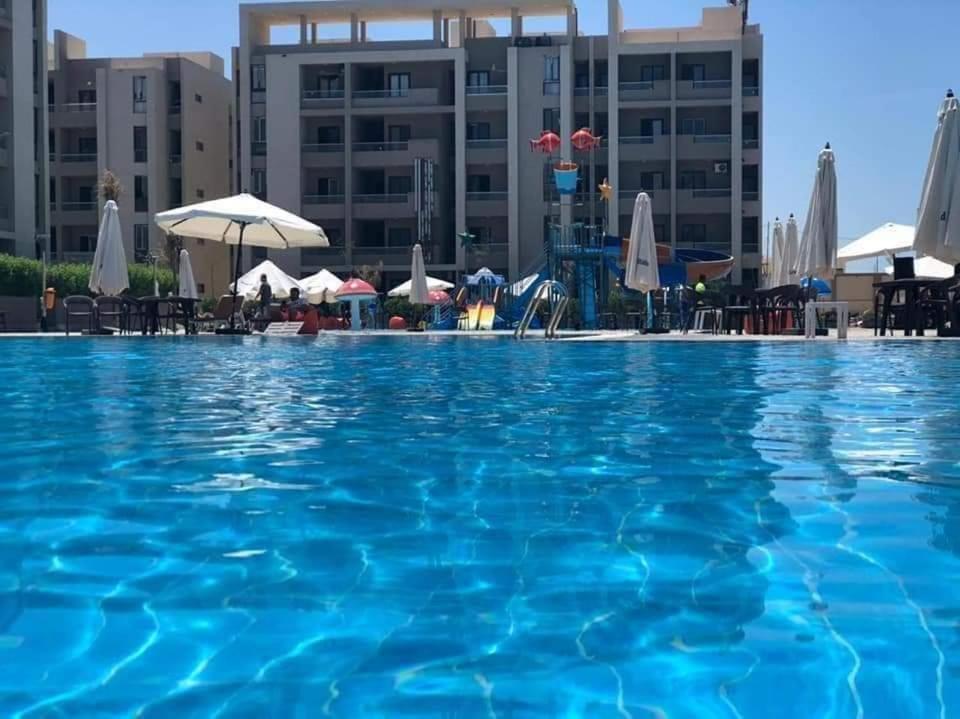 een groot blauw zwembad met tafels en parasols bij قريه جراند هليز in Dawwār ‘Abd Allāh