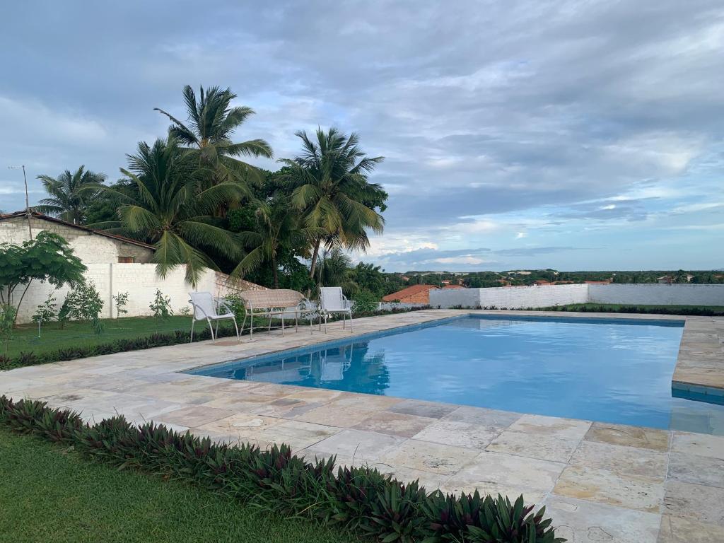 a swimming pool with two chairs and palm trees at CAMA & CAFÉ BED & BREAKFAST HOSPEDARIA MORRO BRANCO 3 MIN A PÉ DAS FALÉSIAs 2 QUADRAS DA PRAIA 1 QUADRA DO MIRANTE & FEIRINHA in Beberibe