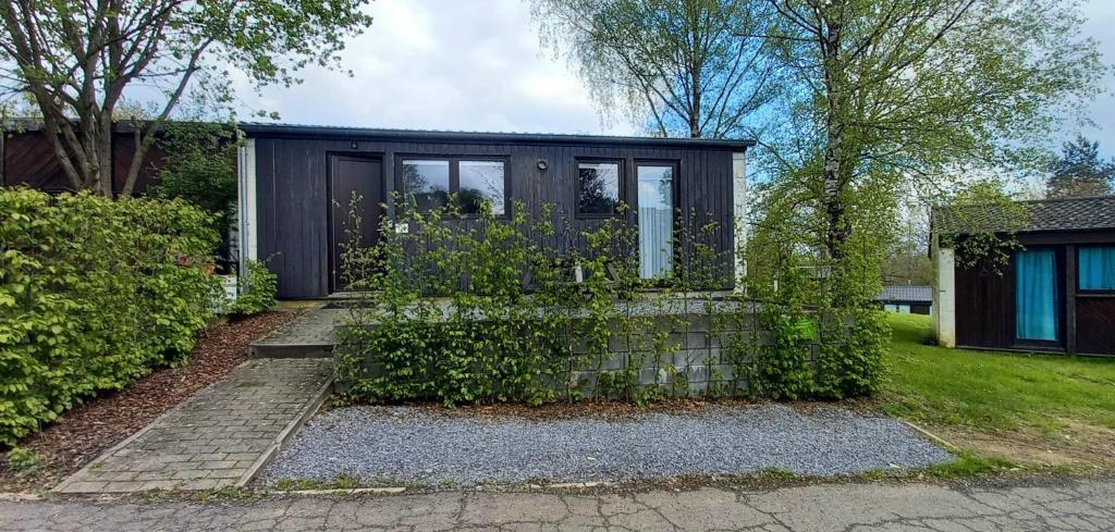 une petite maison noire avec des fenêtres et des buissons dans l'établissement Chalet l'Orvallée, à Virton