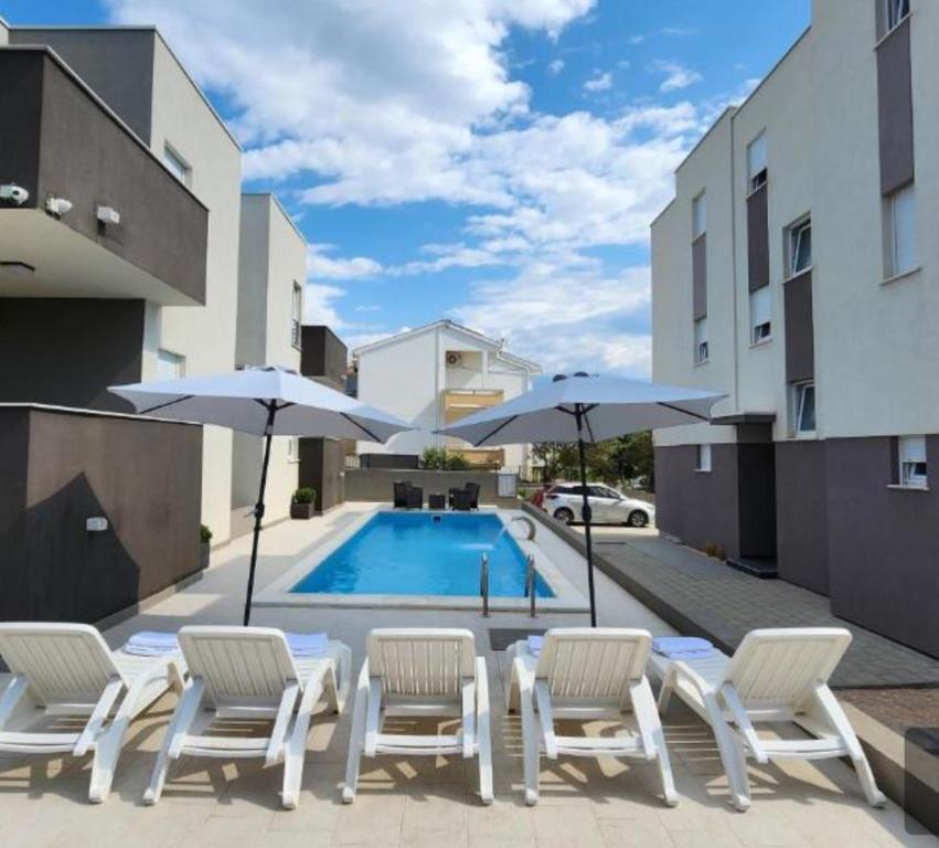 un gruppo di sedie e ombrelloni accanto alla piscina di The Palms Luxury Pool Aparthotel a Novalja (Novaglia)