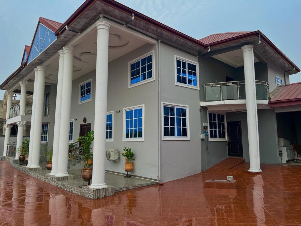 a large white house with columns on a brick floor at EuChris Homes in Kumasi
