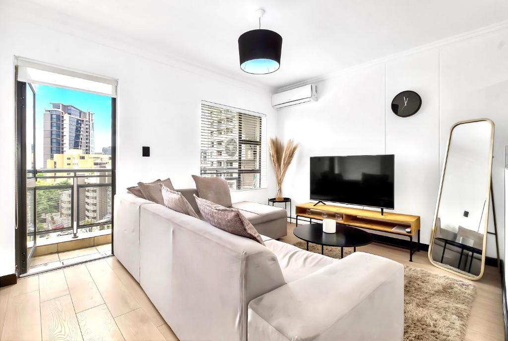 a white living room with a white couch and a tv at Sandton Lux, CBD, 2 Bedroom & 2 Ensuite, No Load shedding in Johannesburg