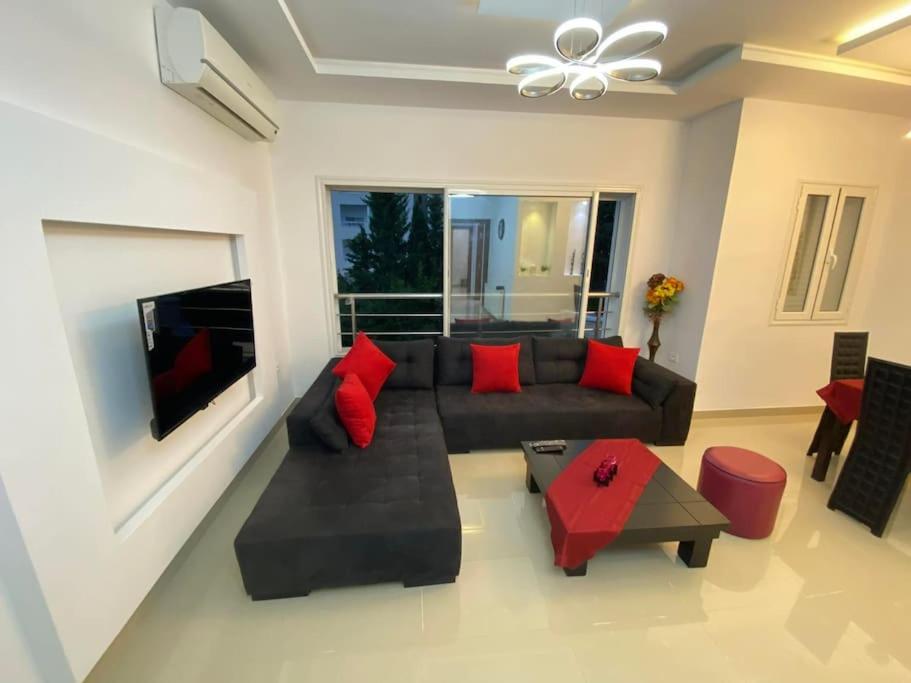 uma sala de estar com um sofá preto e almofadas vermelhas em Nouvel appartement jamais habité em Hammamet Nord