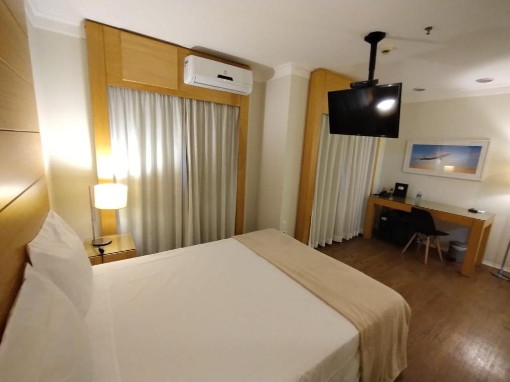 una camera d'albergo con letto bianco e scrivania di H1503 Suíte Luxo Flat Hotel Aeroporto Congonhas a San Paolo