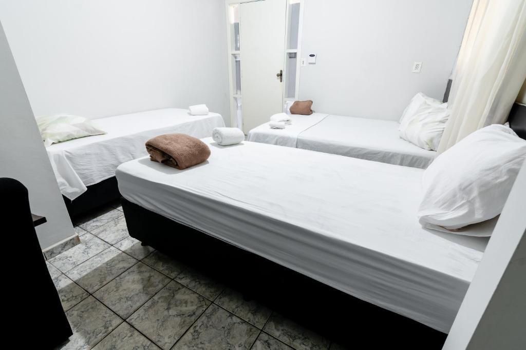 two beds in a room with white sheets and pillows at Quarto 05 Pousada Roosevelt in Uberlândia