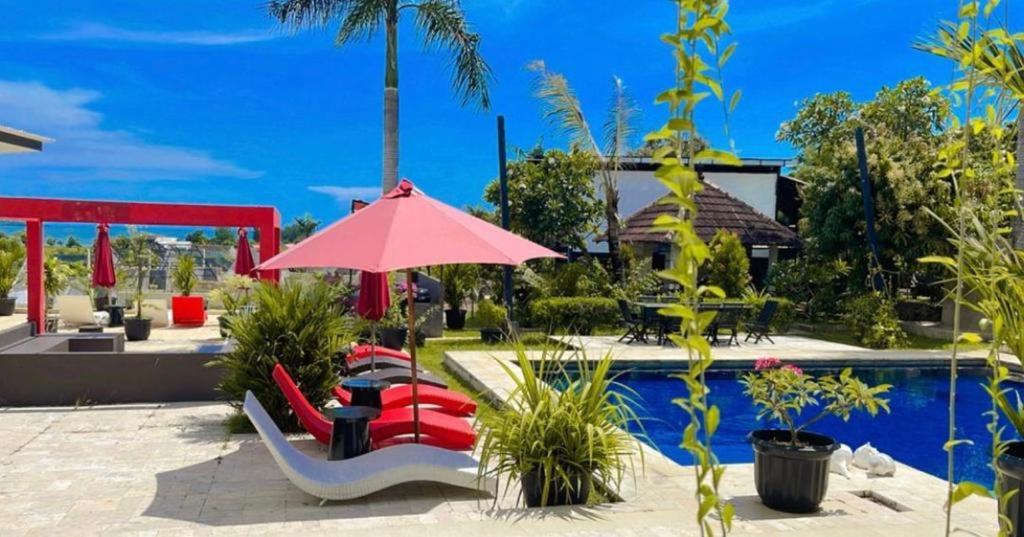 a pool with a red umbrella and chairs and a table at Lucca Resort & Residence in Jepara