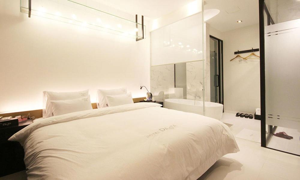 a white bedroom with a large bed and a tub at Jinhae Pasta Hotel in Changwon