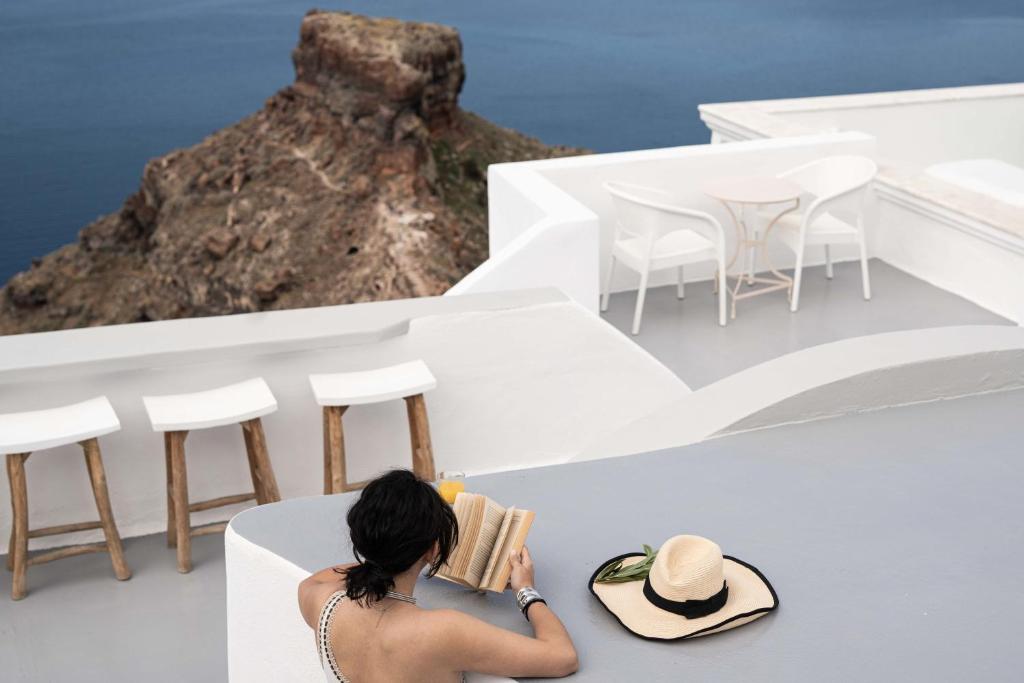 a woman reading a book while sitting on a white building at La Roka, Cliffside Memories in Imerovigli