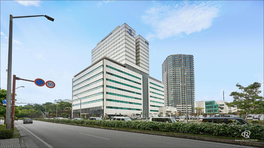 un grand immeuble de bureaux avec des voitures garées devant lui dans l'établissement Daiwa Roynet Hotel Naha Omoromachi, à Naha