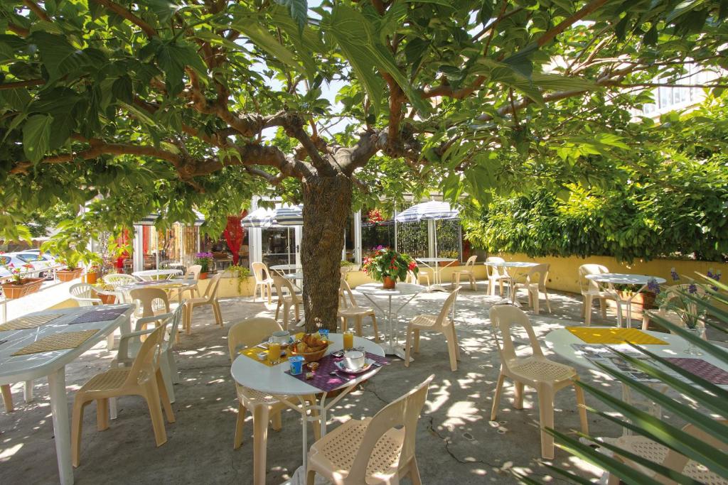 a patio with tables and chairs under a tree at Hôtel La Croix de Malte in La Ciotat