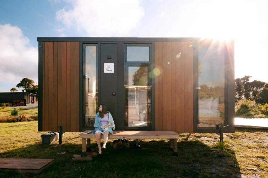 a woman sitting on a bench in front of a tiny house at Rimu View 2 in Ruatapu