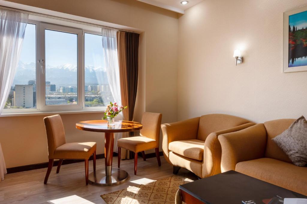 een woonkamer met een tafel en stoelen en een raam bij Regardal Hotel in Alma-Ata