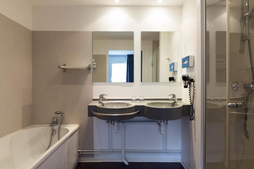 a bathroom with two sinks and a tub and a mirror at The Originals City, Hôtel Acadine, Le Neubourg (Inter-Hotel) in Le Neubourg