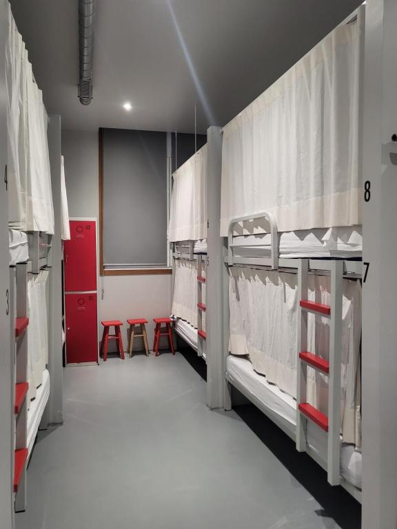 Habitación con 3 literas y 2 taburetes rojos. en Acolá Sport Hostel, en Pontevedra