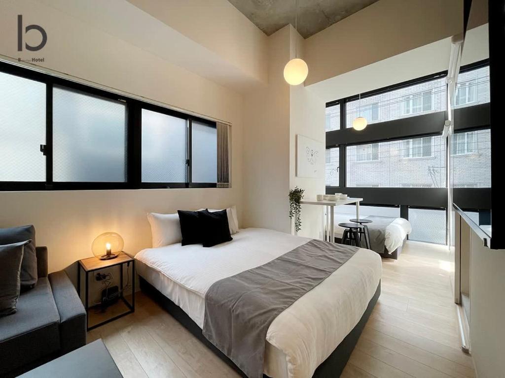 een slaapkamer met een bed, een bank en ramen bij bHOTEL Nekoyard - Brand new 1BR Apt for 7 ppl with loft Few Mins Walk To Peace Park in Hiroshima