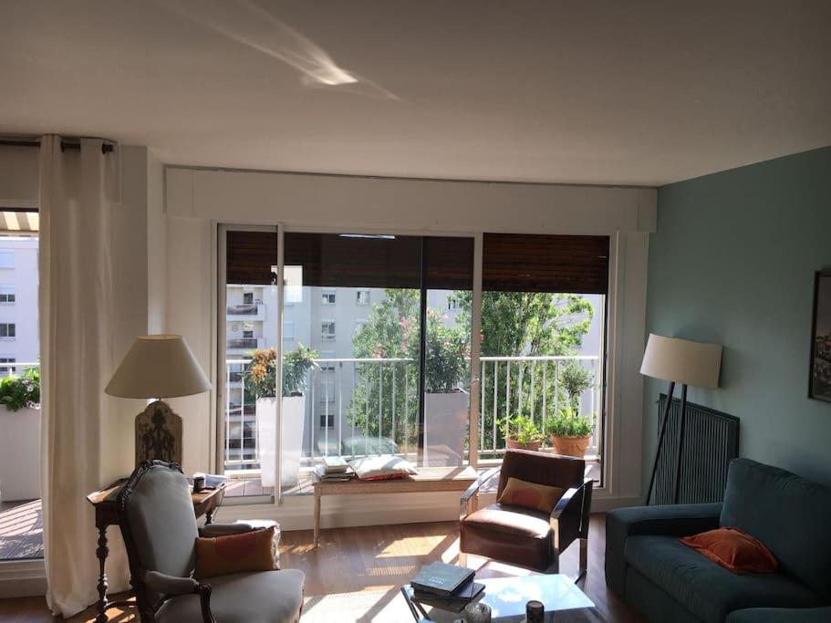 un soggiorno con divano, sedie e una grande finestra di Appartement 70m2 terrasse vue jardin 10min Paris centre a Levallois-Perret