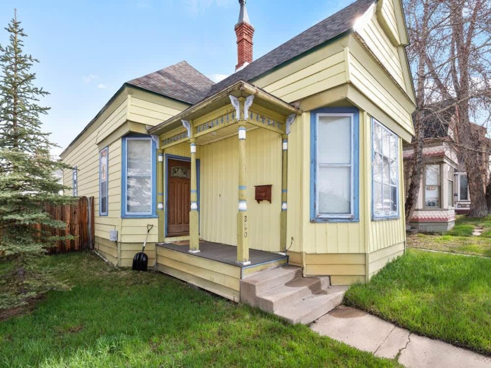 ein kleines gelbes Haus mit einer Veranda und einer Treppe in der Unterkunft The Zinnia Victorian Charm with Mountain Views in Leadville