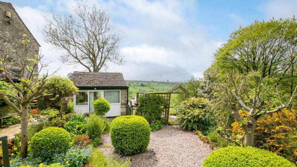 un jardín con arbustos y una casa pequeña en The Potting Shed, en Longnor