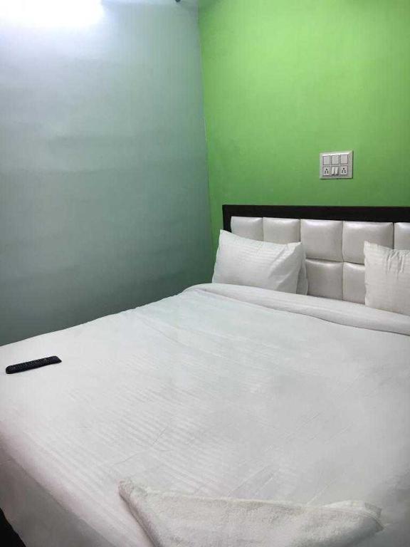 um quarto com uma cama branca e uma parede verde em OYO Hotel The Limestone em Indraprastha