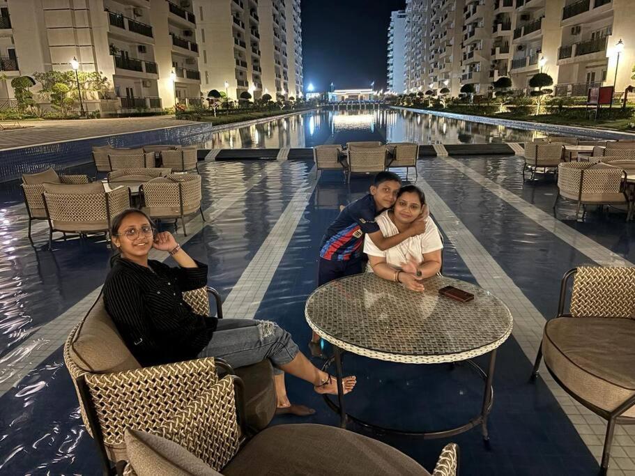 a group of people sitting at a table next to a pool at New 1BHK at Central Park, Sohna Road, Ayaansh Resort in Gurgaon