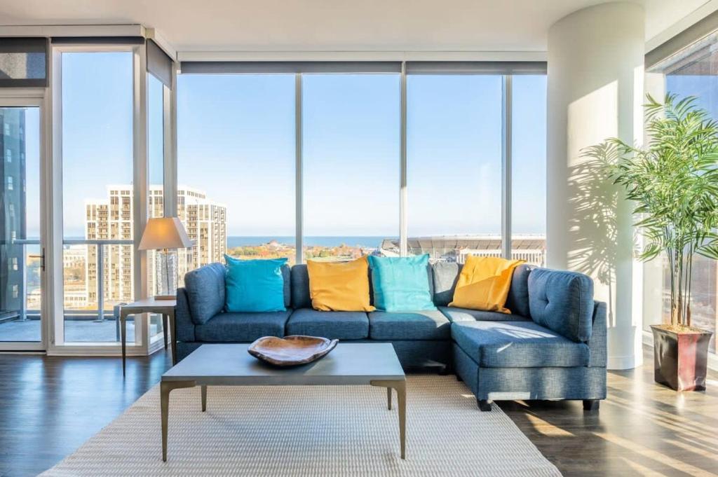 3BR Luxury Glass Apartment With Views Pool & Gym في شيكاغو: غرفة معيشة مع أريكة زرقاء ونوافذ كبيرة