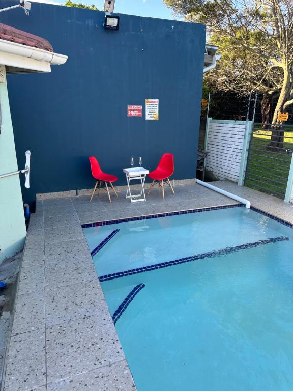 una piscina con 2 sillas rojas y una mesa en The legacy BnB en East London