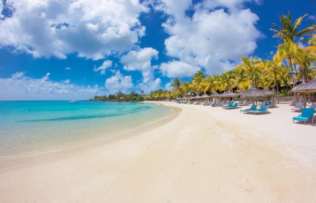 a beach with chairs and palm trees and the ocean at Royal Palm Beachcomber Luxury in Grand Baie