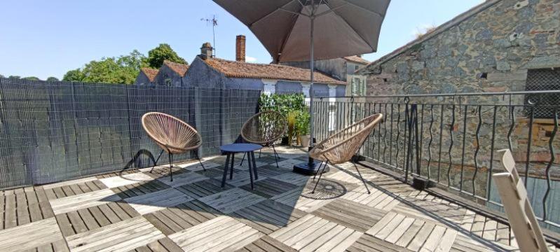 un patio con sillas y una sombrilla en el balcón en Le Refuge du Fou en La Forêt-sur-Sèvre
