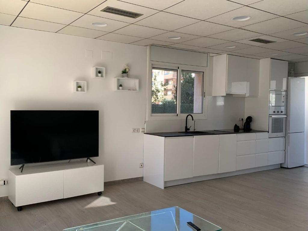 een keuken met witte kasten en een flatscreen-tv bij Apartamento sol y playa in Calafell
