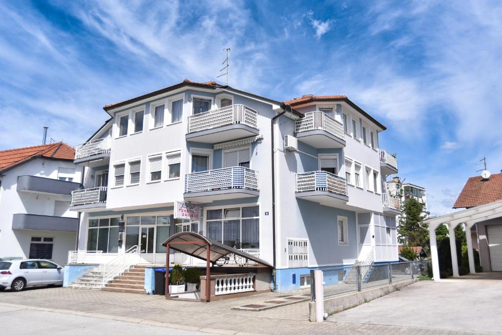 ein weißes Gebäude mit Balkonen und einem Auto, das vor der Tür geparkt ist in der Unterkunft Apartman Podravina in Ludbreg