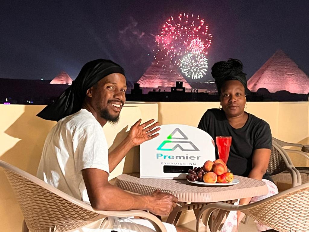 two men sitting at a table with a plate of fruit and fireworks at Premier Pyramids INN in Cairo