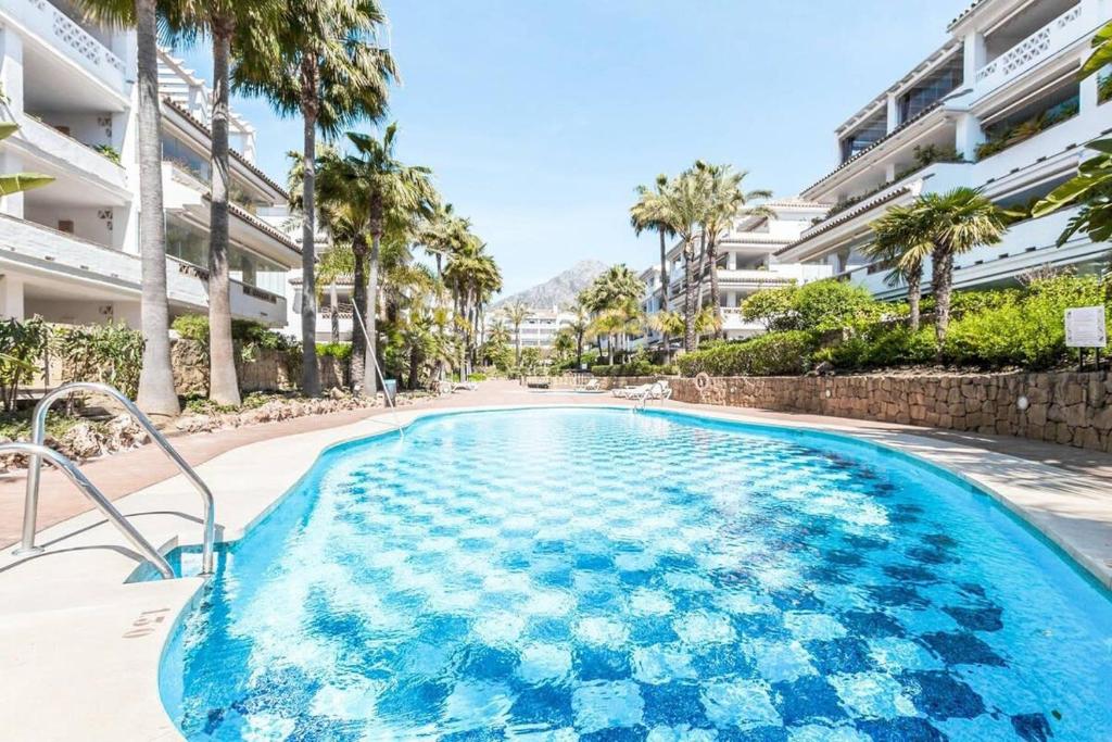 una piscina con palmeras y edificios en BEACHFRONT GOLDEN MILE PUENTO ROMANO SEA VIEW WIFI, en Marbella