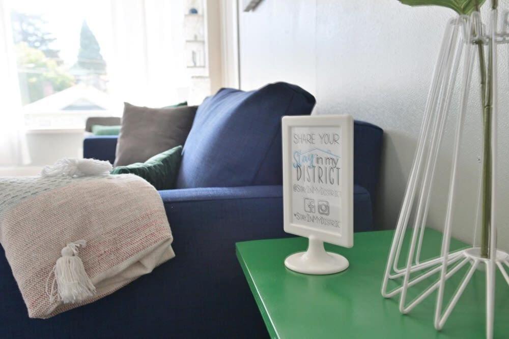 a living room with a blue couch and a sign on a table at #StayinMyDistrict Heritage House Private Suite in Coos Bay