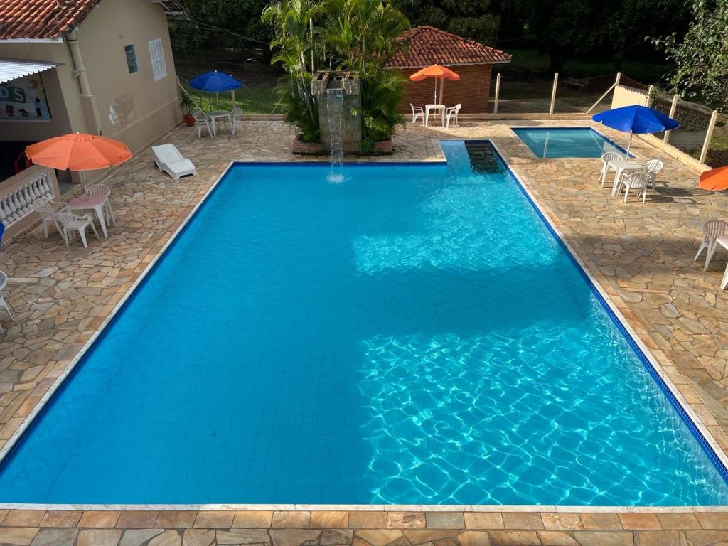 a large blue swimming pool with chairs and umbrellas at Pousada Ananda São Pedro in São Pedro
