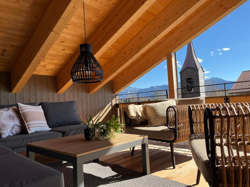 a porch with couches and a table and a church at Chiemgauloft , 5 Sterne Ferienwohnung am Chiemsee in Übersee