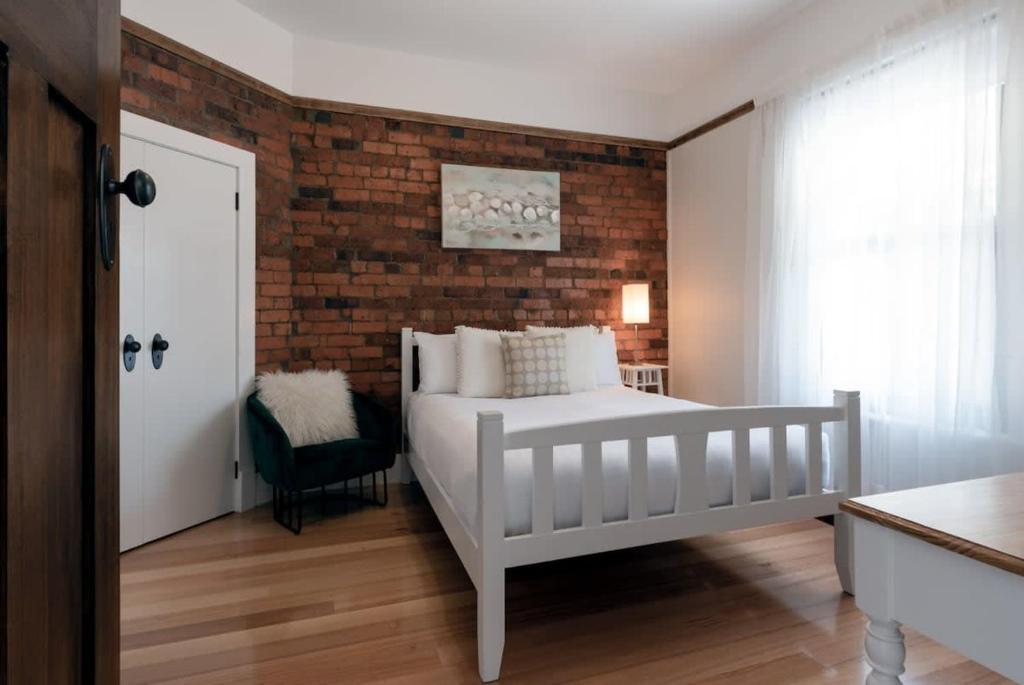 a bedroom with a white bed and a brick wall at Cosy Accommodation Moments From The Centre Of Town with Wifi in Launceston