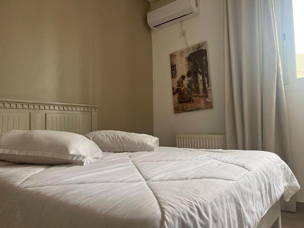 Hotel Transatlantique Tunis في تونس: غرفة نوم بسرير وملاءات بيضاء ونافذة