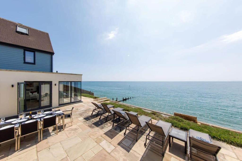 a patio with tables and chairs next to the ocean at The Sea House - Ultimate Seafront Living & Sunsets in Selsey
