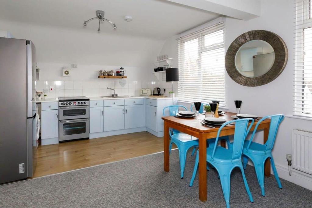 cocina con mesa de madera y sillas azules en Two-bed beachside apartment West Wittering, en West Wittering