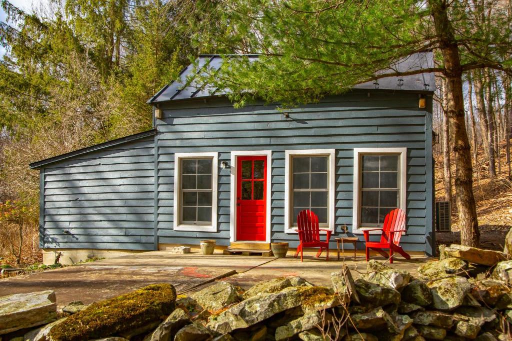 ein kleines blaues Haus mit einer roten Tür und zwei Stühlen in der Unterkunft Catskills Cabin on Wooded 100 Acres with Lake in West Coxsackie