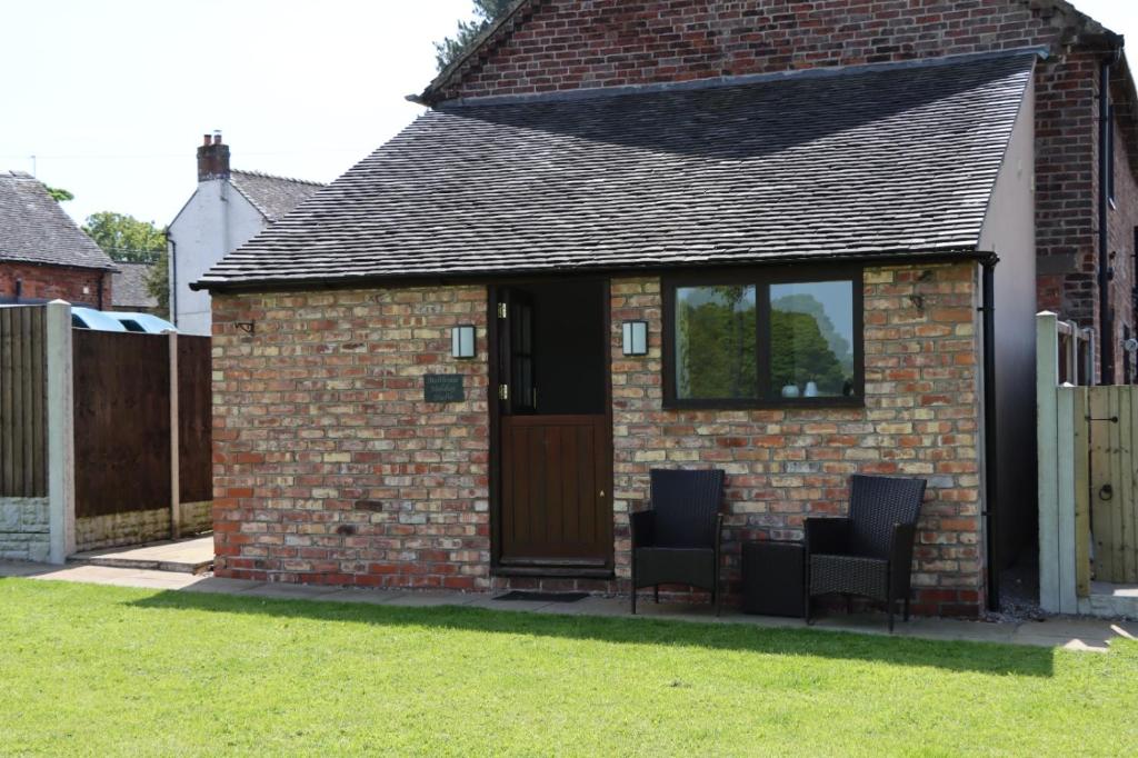 uma pequena casa de tijolos com duas cadeiras e uma porta em Malthouse Farm Cottage Studio em Dilhorne