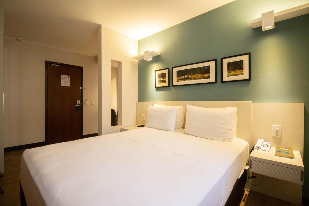 une chambre avec un lit blanc avec un mur vert dans l'établissement Charmoso e central, à Brasilia