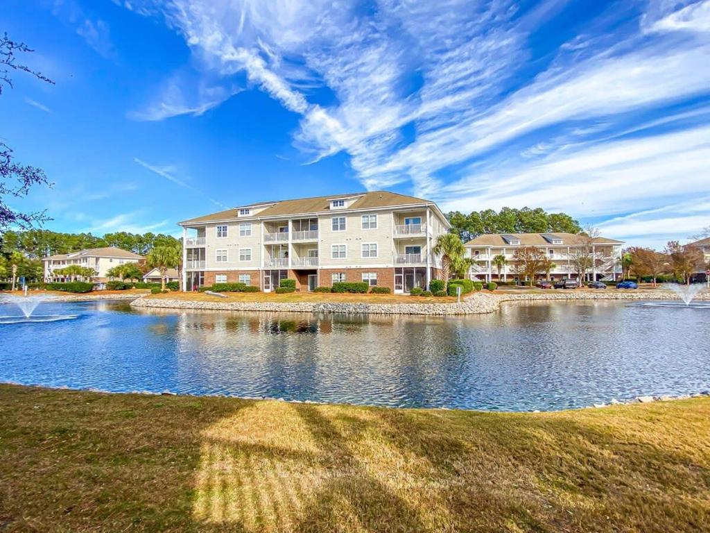 a large apartment building with a lake in front at Lakefront at Barefoot Resort w Massive Waterfront Pool Close to Beach in North Myrtle Beach